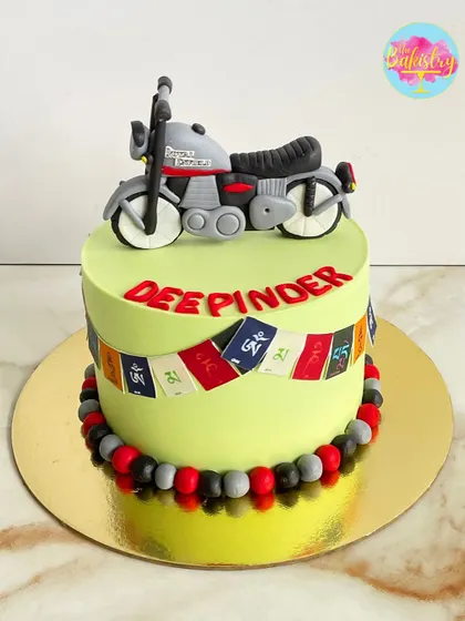 A cake for a biker who loves to travel. This Royal Enfield-themed cake features a handcrafted 3D bike topper and Tibetan prayer flags for that authentic traveler feel.