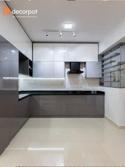 This L-shaped kitchen uses a sophisticated grey and white color palette with a high-gloss finish. The open shelving on the side adds visual interest and breaks the monotony of closed cabinets, blending storage and style.