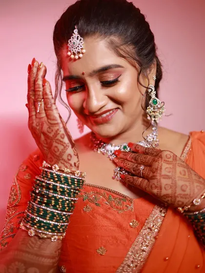 Hamsa's reception look, featuring a vibrant orange lehenga. Her makeup is glowing and happy, with a focus on her bright smile and sparkling eyes.