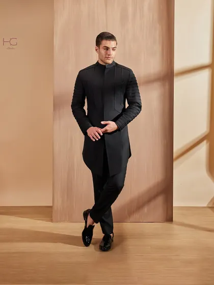 This pose highlights the architectural quality of the pleated sleeves and the asymmetric cut of the achkan, a fusion of classic tailoring and avant-garde design.