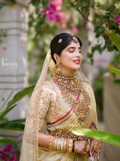 A serene bridal portrait amidst lush greenery. The natural light beautifully catches the glow of her skin and the intricate details of her temple jewellery.