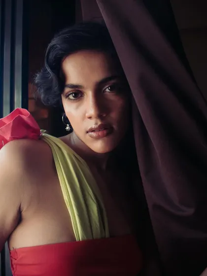 An intimate close-up portrait, with the model partially hidden by a curtain. The soft, natural light and gentle expression create a warm and inviting mood.