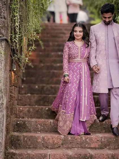 The couple descends a rustic stone staircase hand-in-hand, their elegant pastel outfits creating a beautiful picture of romance.