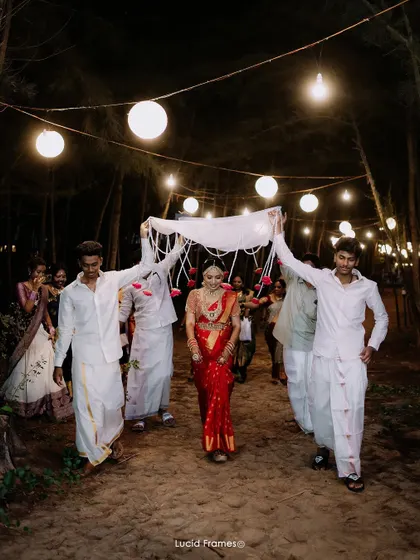 The bride's grand entrance at night, guided by family under a canopy of cloth and lights.