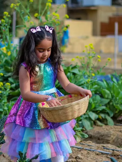 A young girl in a rainbow dress carefully collecting her harvest in a small basket.