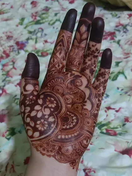 A beautiful, dark henna stain on the palm. The floral and paisley patterns are clearly defined by the rich color.