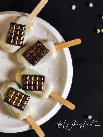 White chocolate-coated cakesicles decorated with a mini chocolate bar on top. A fun and creative design for chocolate lovers.
