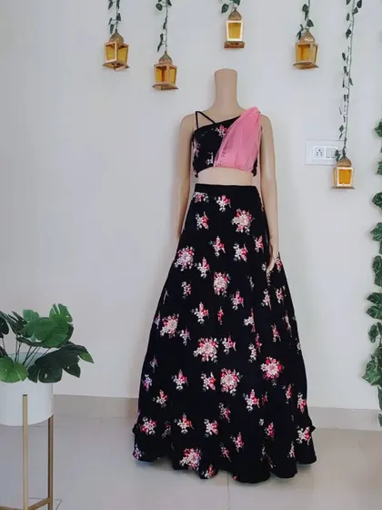 A custom-designed black lehenga with colorful floral embroidery. The one-shoulder blouse with a sheer pink drape adds a modern and unique touch.