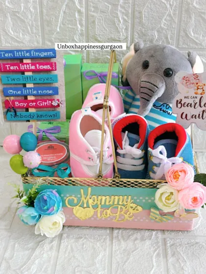 Another angle of the gender-reveal hamper, showcasing the arrangement of the plush elephant, colorful sign, and two pairs of baby shoes, all within a beautifully decorated basket.