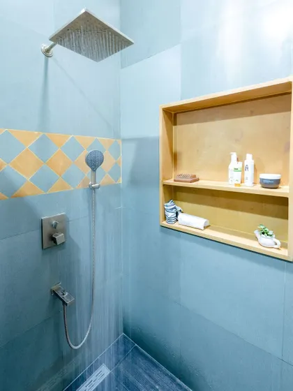 A simple yet elegant shower area with grey tiles and a patterned accent strip, complemented by a wooden storage niche.