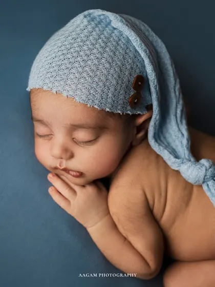 A bundle of joy in baby blue. This newborn is wearing an adorable knotted hat, adding a whimsical touch to this classic sleepy portrait.