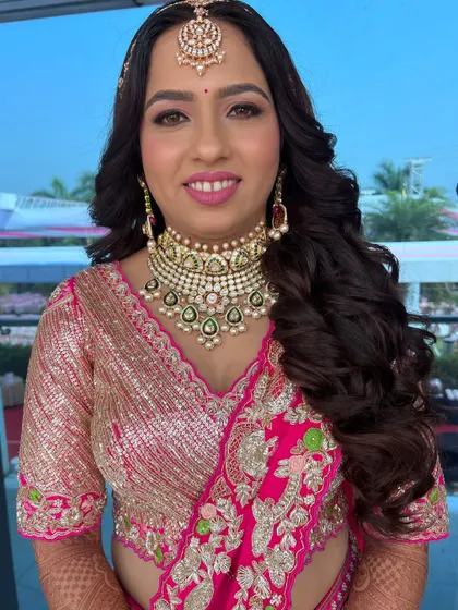 A beautiful bride in a pink and gold lehenga. The makeup is soft and glamorous, with voluminous waves for a modern touch.