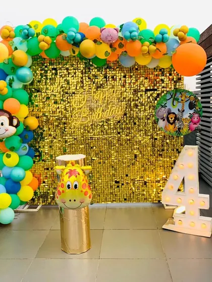 A rooftop jungle-themed party for a 4th birthday. The setup includes a gold shimmer wall, a colorful balloon arch, and large cutouts of an elephant and giraffe.