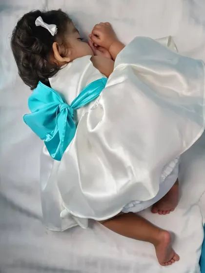 A sleeping angel in her beautiful white satin dress. This image highlights the soft, comfortable fabric and the lovely oversized bow in the back.