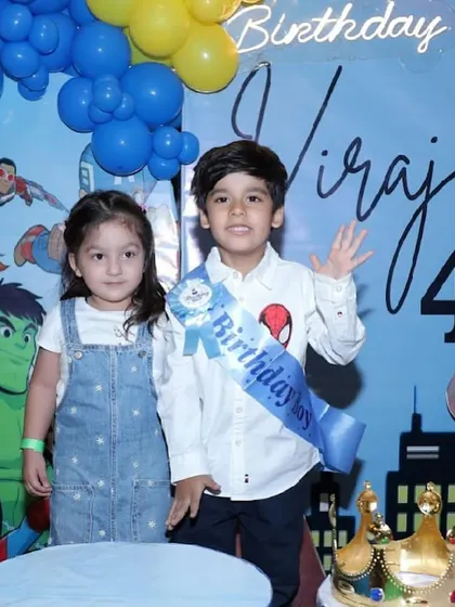 The birthday boy and his little sister pose in front of the vibrant superhero backdrop at his 4th birthday party.