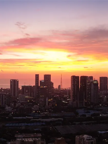 A beautiful shot of the Mumbai skyline silhouetted against a bright, fiery sunset, highlighting the density of the city's architecture.