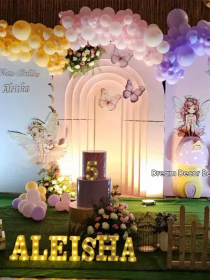 A beautiful fairy-themed fifth birthday party. The backdrop features pastel arches and balloons, with delicate fairy cutouts and a custom cake stand.