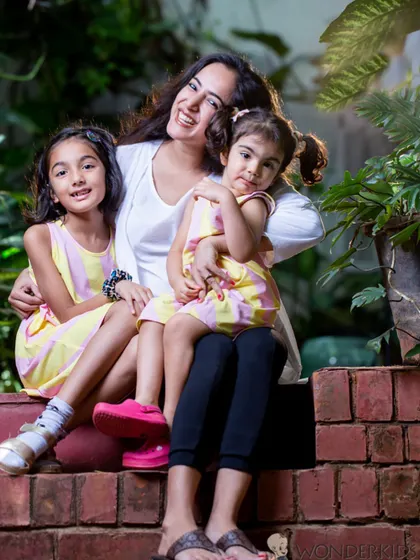 A mother relaxes with her two daughters in a lush garden setting. Their natural smiles and the beautiful greenery create a warm and candid family portrait.