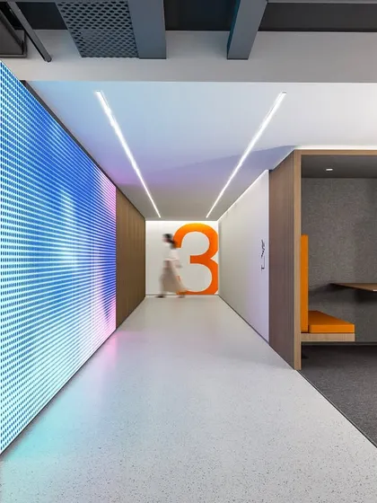 A view showing the juxtaposition of different functional zones: a dynamic LED wall, informational displays, and cozy collaboration booths. The design uses color and light to define spaces and guide movement, proving that a workplace can be fun and progressive without being pretentious.