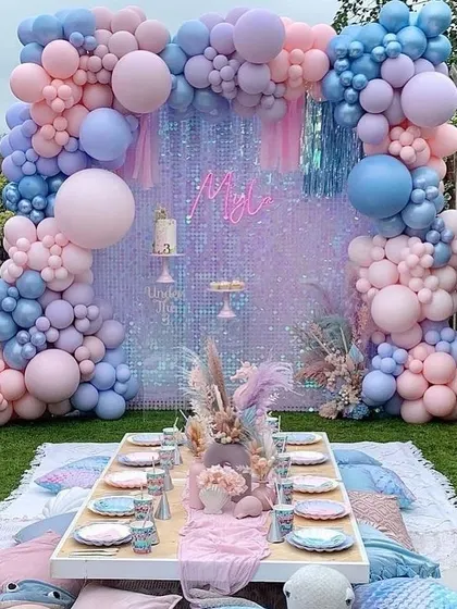 A dreamy pastel-themed picnic setup for a kid's birthday party. The low table, floor cushions, and iridescent sequin backdrop create a magical and fun atmosphere.