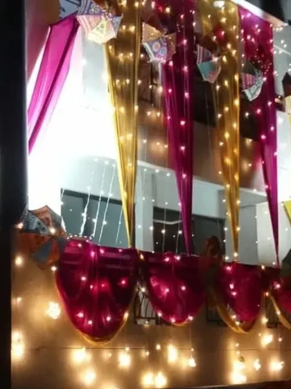 A nighttime shot of balcony decoration, where pink and yellow drapes are interwoven with bright fairy lights.