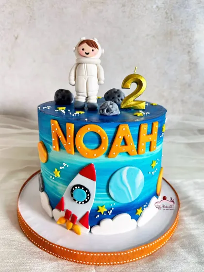 A birthday blast-off! This space-themed cake features a little astronaut, a rocket ship, and planets, all on a beautiful blue galaxy-painted buttercream.
