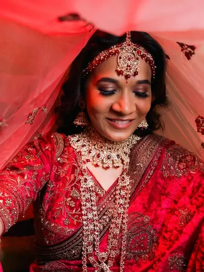 A bride lifts her red veil, revealing a beautiful smile.