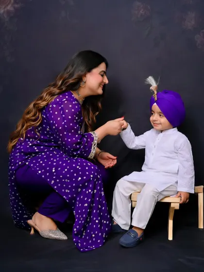 A mother shares a sweet, interactive moment with her son, who is dressed in a traditional kurta and turban. This photo highlights the beautiful bond between mother and child.