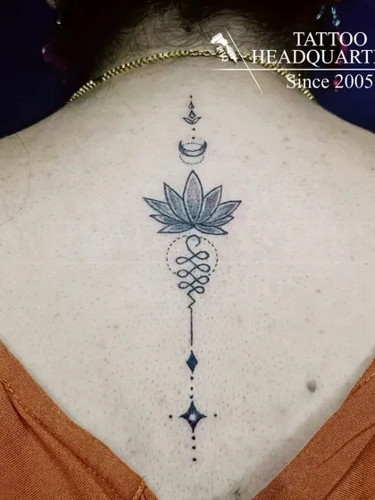 A beautiful Unalome tattoo on the spine, symbolizing the path to enlightenment. The design incorporates a lotus flower, representing purity and spiritual awakening.