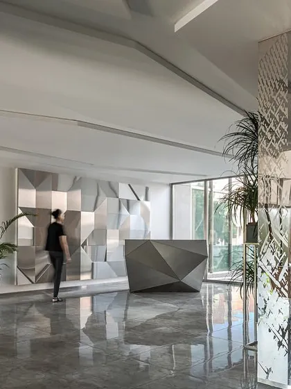 The main reception area of the Stainless Steel Office features an angular, custom-designed stainless steel desk set against a matching feature wall, creating a cohesive and modern first impression.