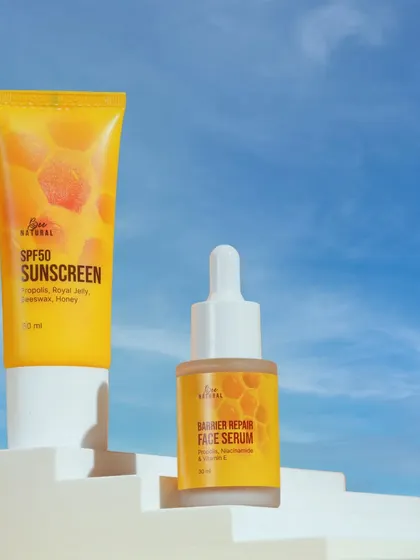 A honey-based sunscreen and serum duo, shot against a bright blue sky. This setup communicates sun protection and a fresh, airy feel.