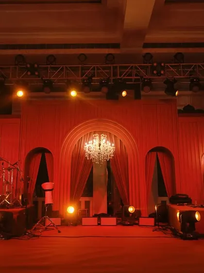 The stage for the evening's entertainment, washed in a warm red glow. The arched backdrop and crystal chandeliers add a touch of classic elegance to the modern monochromatic theme.
