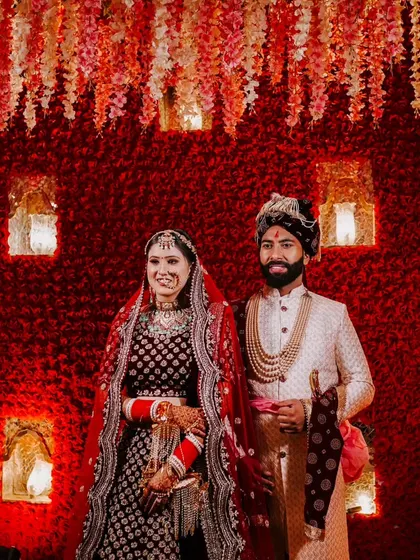 A classic wedding portrait against a dramatic red backdrop. The couple stands together, showcasing their regal wedding attire.