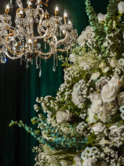 A close-up of a chandelier and a large white floral arrangement. The warm light from the chandelier beautifully illuminates the flowers, making them glow.