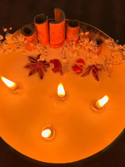An overhead shot of the 6-inch urli candle, glowing warmly in a dark room. The spices and botanicals create beautiful silhouettes.