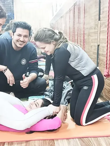 Teamwork makes the dream work. Students help each other achieve Yoganidrasana (Yogic Sleep Pose) under the watchful eye of an instructor.