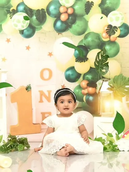 A beautiful portrait before the cake smash begins. The jungle-themed setup with green balloons and monstera leaves creates a fresh, vibrant atmosphere.