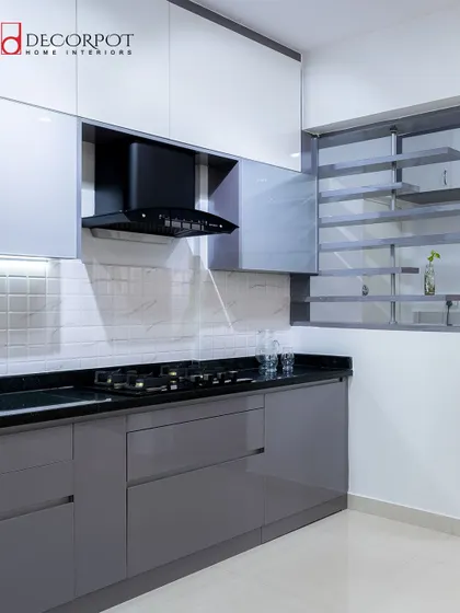 This L-shaped kitchen uses a modern grey and white color scheme. The open shelving unit built into the window space is a clever way to add storage without blocking natural light.