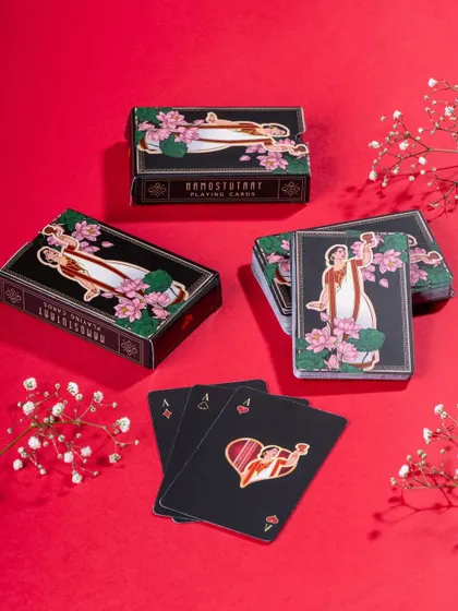 A vibrant flat lay of Namostutay playing cards against a bold red background. The styling with delicate white flowers provides a beautiful contrast and highlights the product's artistic design.