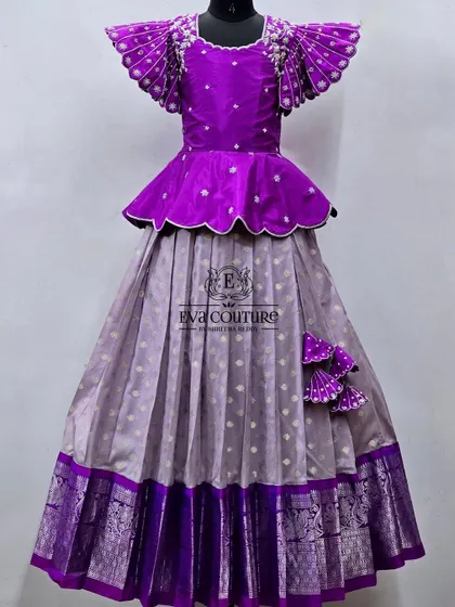 A unique designer lehenga with dramatic wing-like sleeves. The purple peplum top is paired with a grey silk skirt with a purple zari border, creating a very modern and stylish outfit.