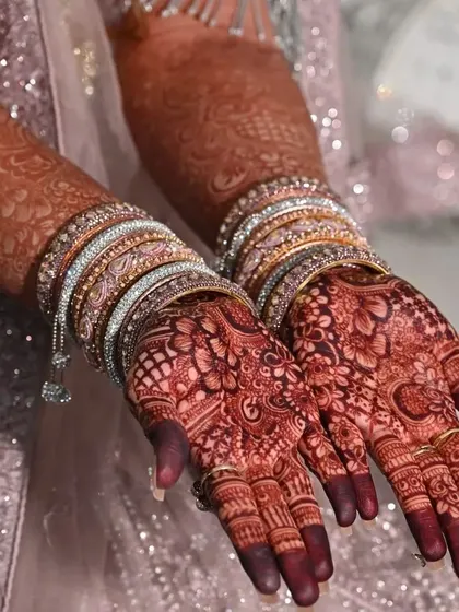 A candid shot of a bride's hands, showing the beautiful dark stain of her henna, adorned with sparkling bangles.