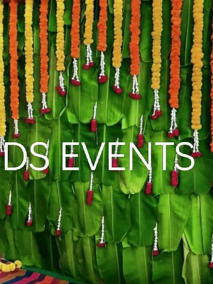 A close-up of a backdrop made from fresh banana leaves. The vibrant green is complemented by hanging garlands of orange and yellow marigolds, creating a fresh and traditional look for any auspicious event.