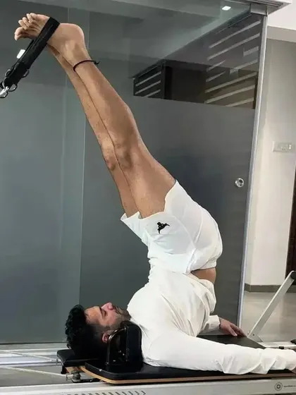 Varun Dhawan performing an inversion on the Reformer. This advanced move is excellent for spinal decompression and building core strength, demonstrating the versatility of Pilates for men.