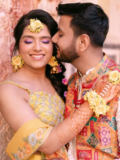 A sweet, candid moment during the Haldi ceremony, with the groom whispering in the bride's ear, making her smile.