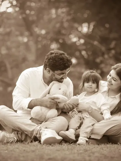 The family plays with a stuffed bunny during their picnic-style photoshoot in the park. A lovely sepia-toned image.