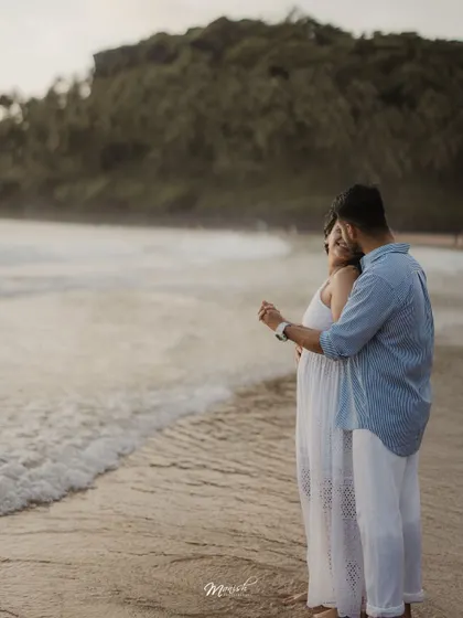 An embrace from behind as they watch the waves, a classic and heartwarming portrait of love by the sea.