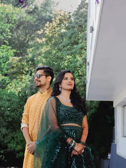 A beautifully composed portrait of the couple standing back-to-back, looking towards their future. The natural lighting and green surroundings create a fresh and hopeful mood.