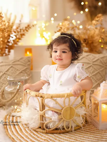 A happy little girl in a wicker basket, surrounded by the warm glow of candles and fairy lights in a beautiful boho-themed first birthday session.