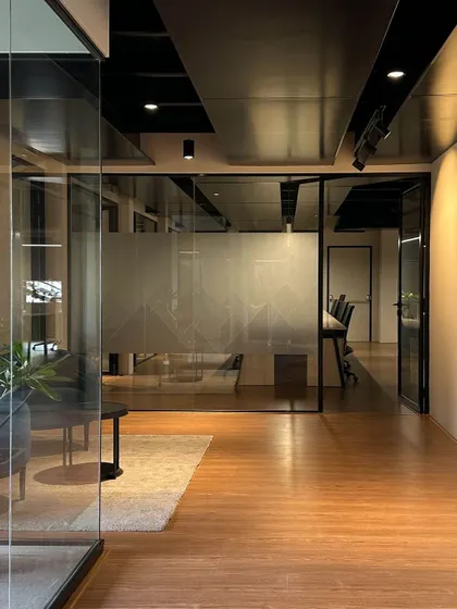 A transitional space featuring a frosted glass wall with a geometric pattern. This element provides privacy for the adjoining meeting room while allowing light to filter through, maintaining a bright and open feel in the hallway.