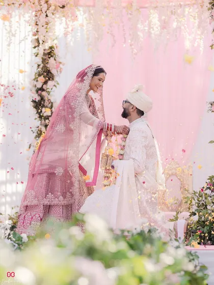 A beautifully framed shot of the Varmala ceremony, with soft flowers in the foreground adding depth and romance to this key wedding moment.